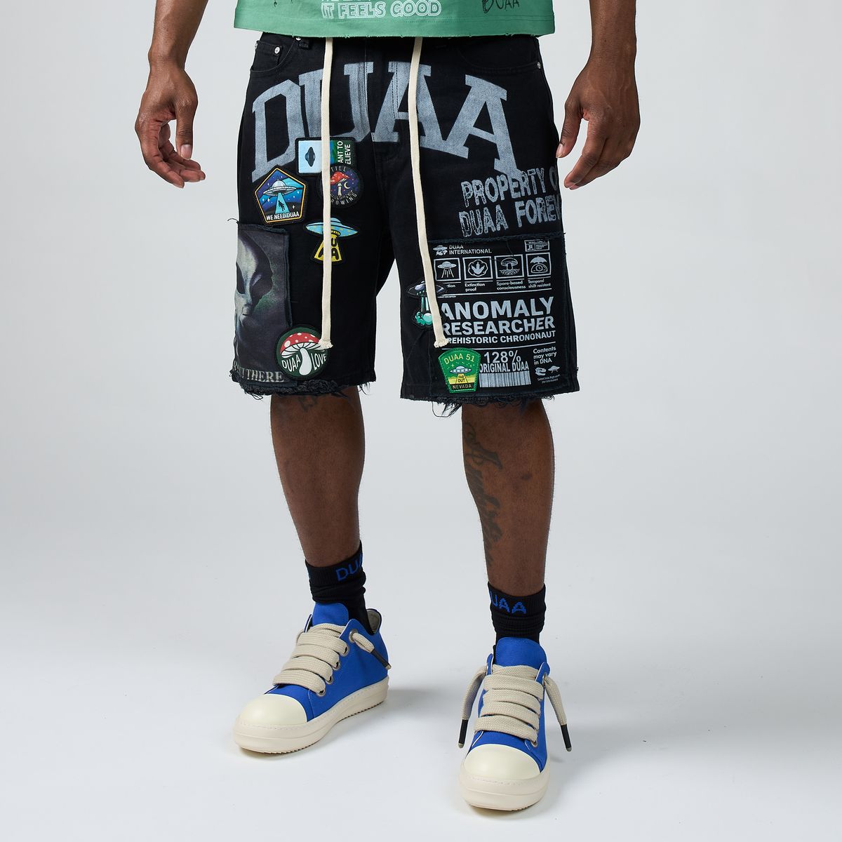 Men’s black graphic shorts with large front patch panels and distressed edges
