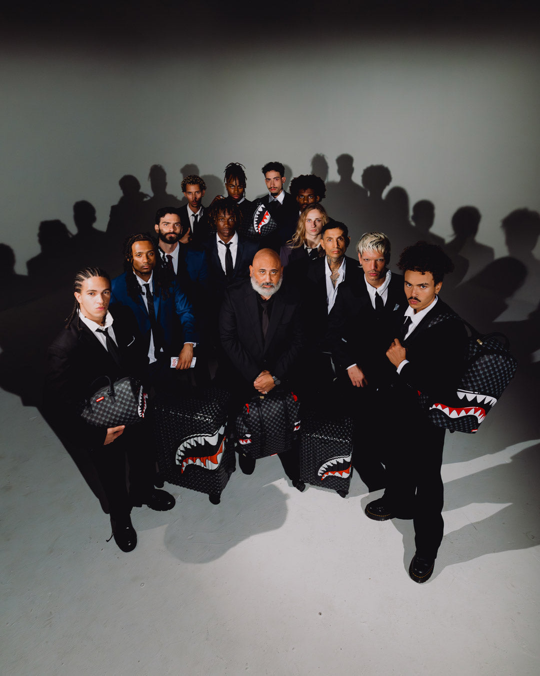 Sprayground shark-mouth backpack bag among group posing, black with red/white design