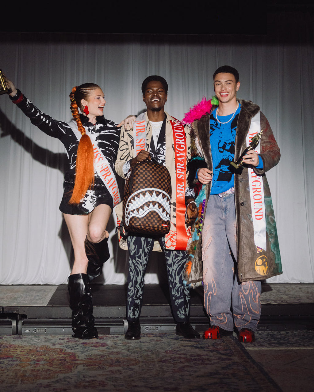 Brown checkered backpack with white graphic worn by model on stage