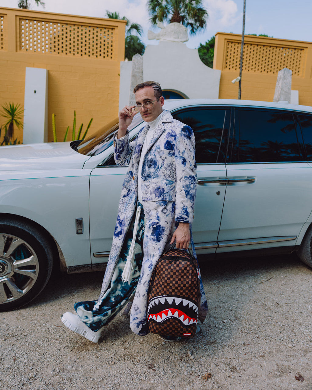 Backpack with shark-mouth graphic on the ground next to a person by a car