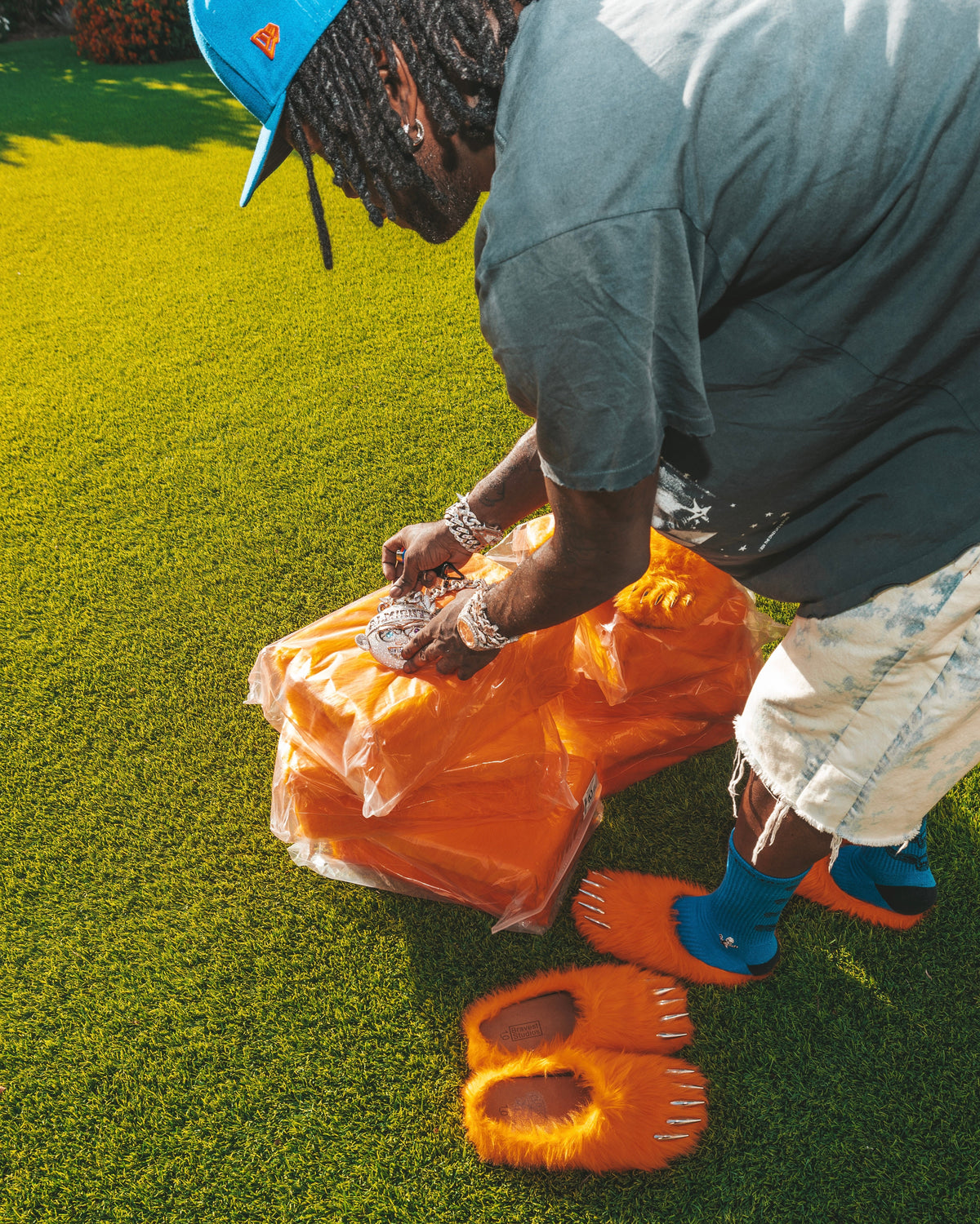 Orange plush bear-claw slippers on grass, with orange packaged pairs held nearby.