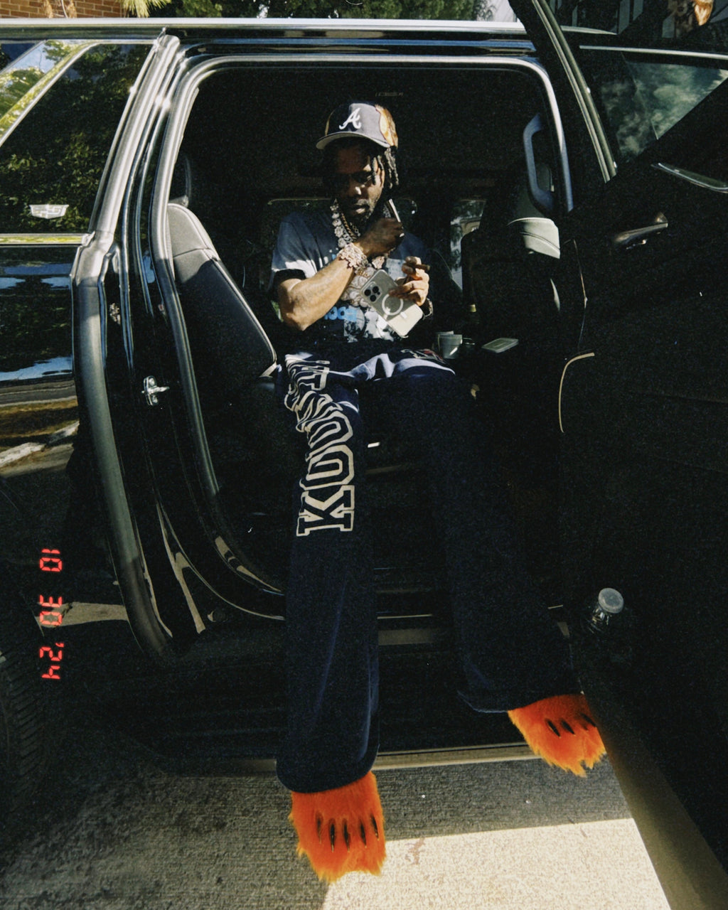 Orange plush bear-claw slippers worn with dark pants, dangling from an open car door.