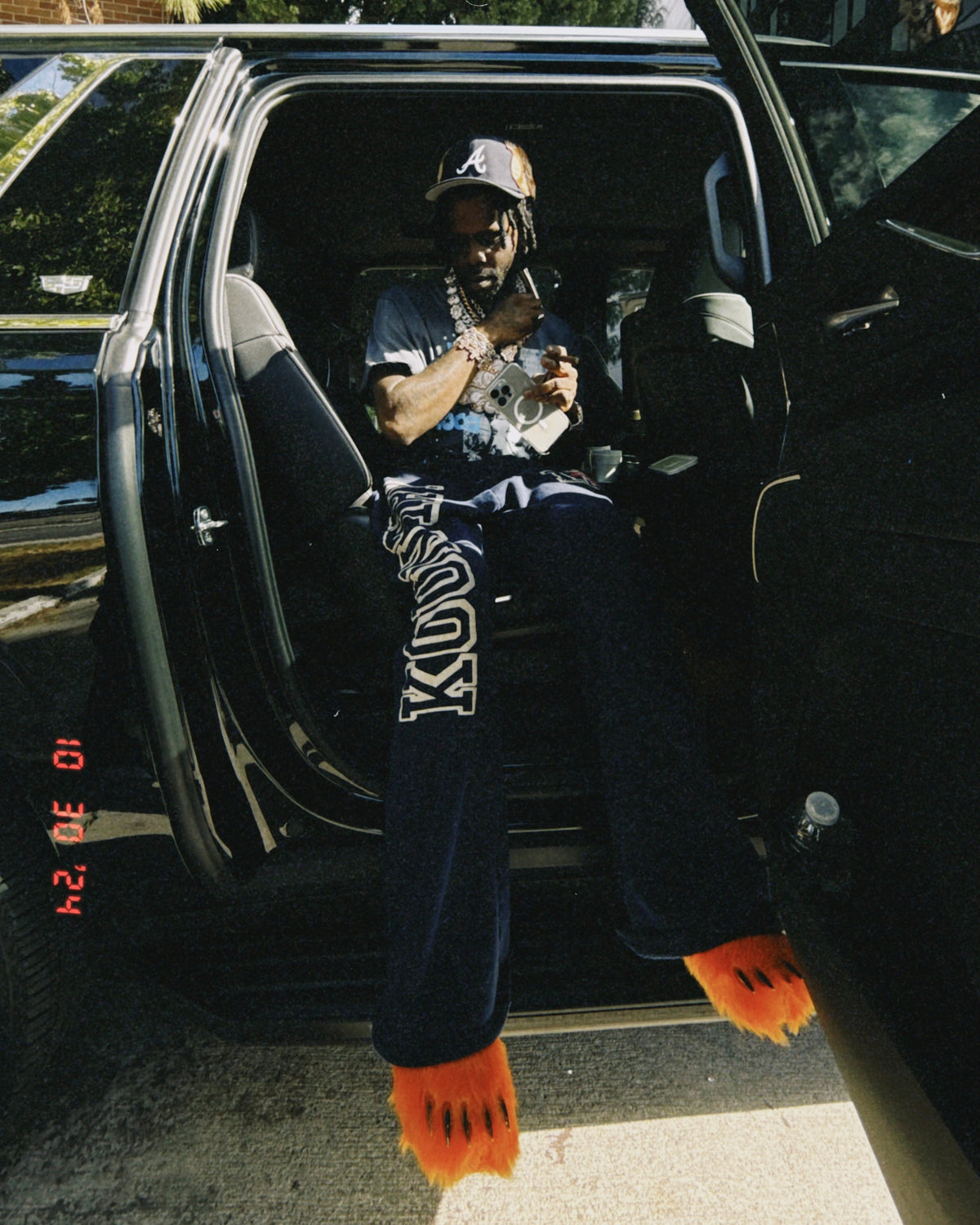 Orange plush bear-claw slippers worn with dark pants, dangling from an open car door.