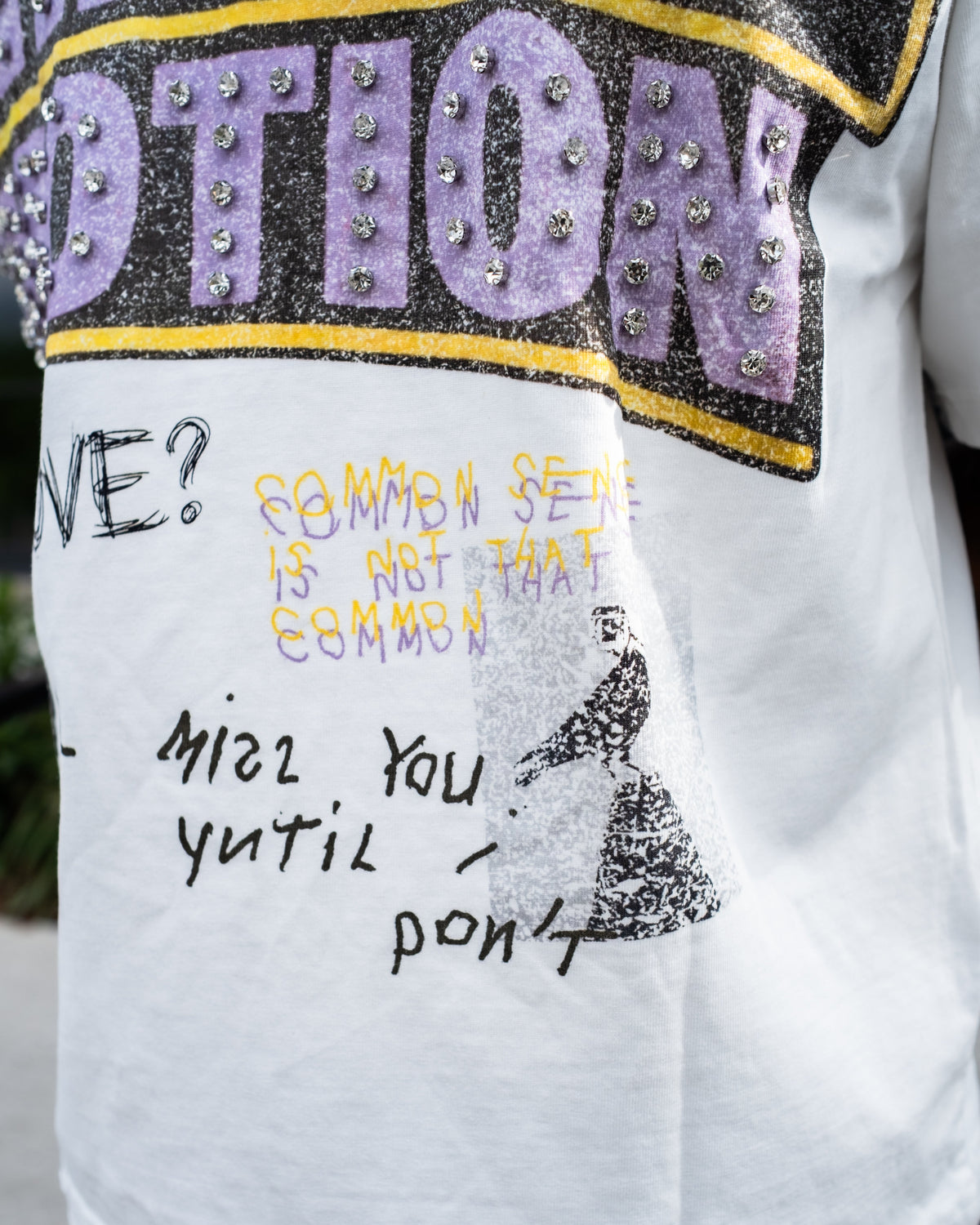 Men's white T-shirt close-up of 'Mixed Emotion' purple-and-gold graphic lettering