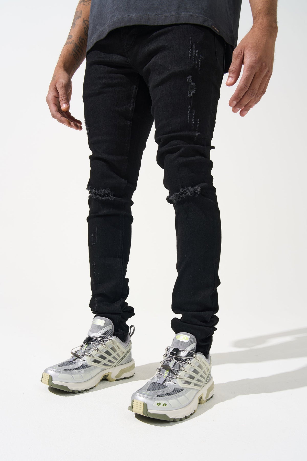 Men's black denim jeans with distressed knee patches and tapered leg openings