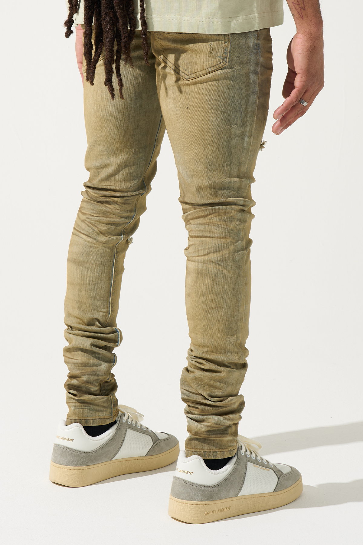 Men's skinny jeans in muted olive with worn front legs, cuff wrinkles, and small side distress