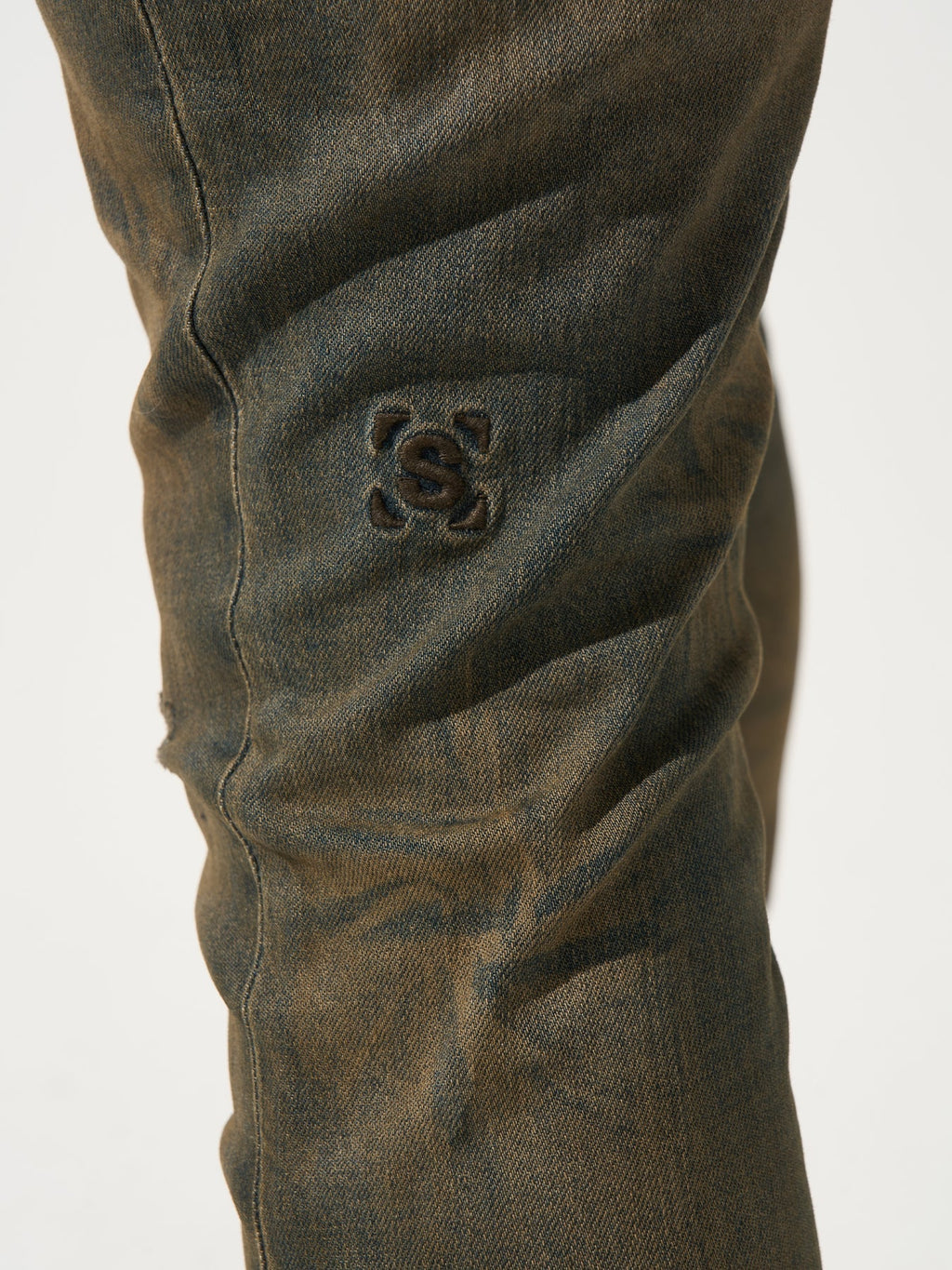 Earth-brown denim jeans close-up of back pocket logo patch.