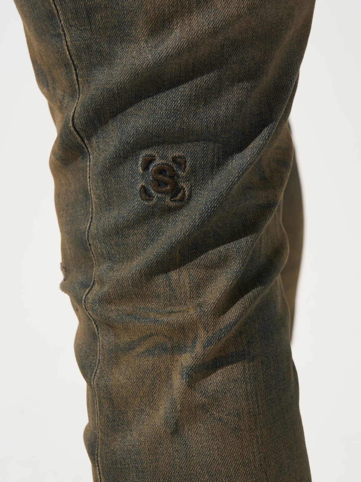 Earth-brown denim jeans close-up of back pocket logo patch.