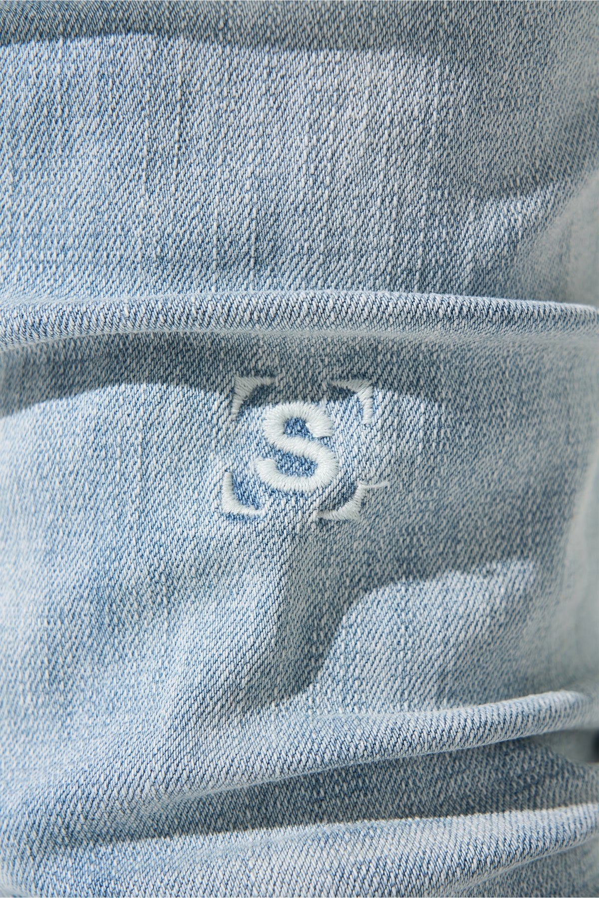 Light blue denim jeans close-up of back pocket with stitched 'S' logo