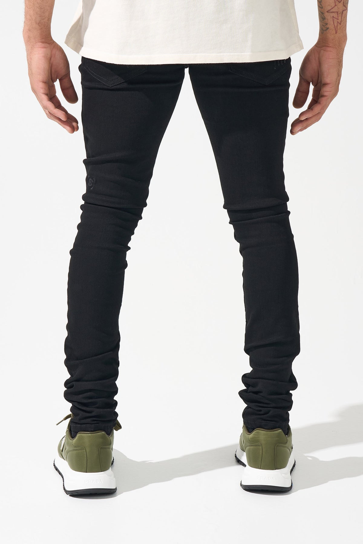Men's black distressed denim jeans with worn knee patches and tapered legs