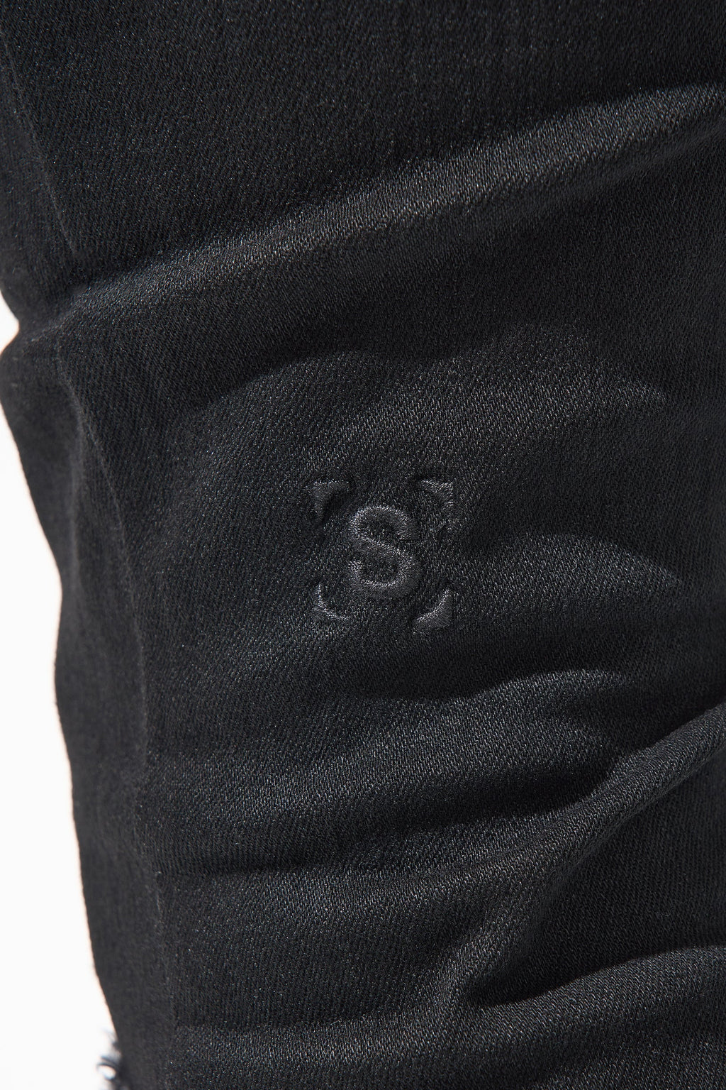 Jet black jeans fabric detail with subtle stitched logo on thigh