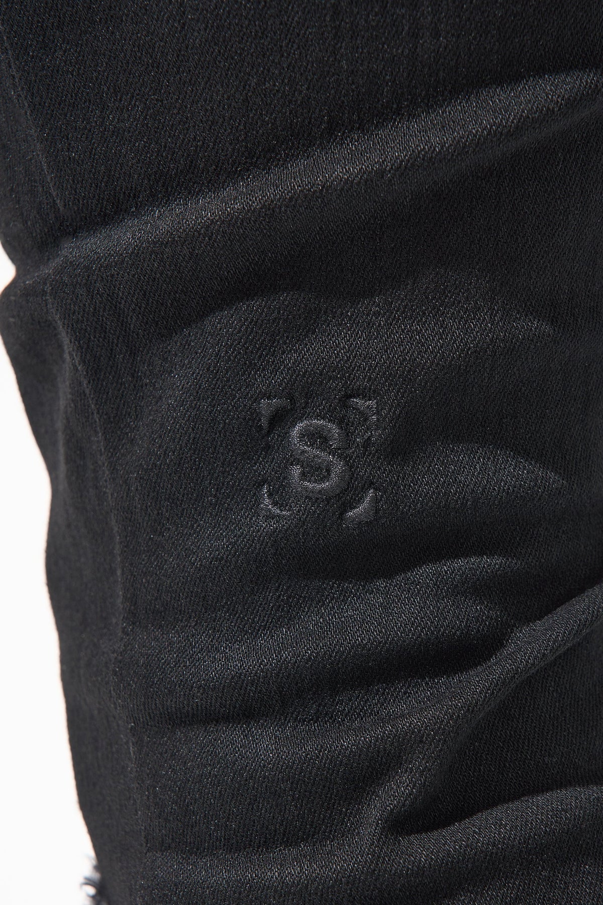 Jet black jeans fabric detail with subtle stitched logo on thigh