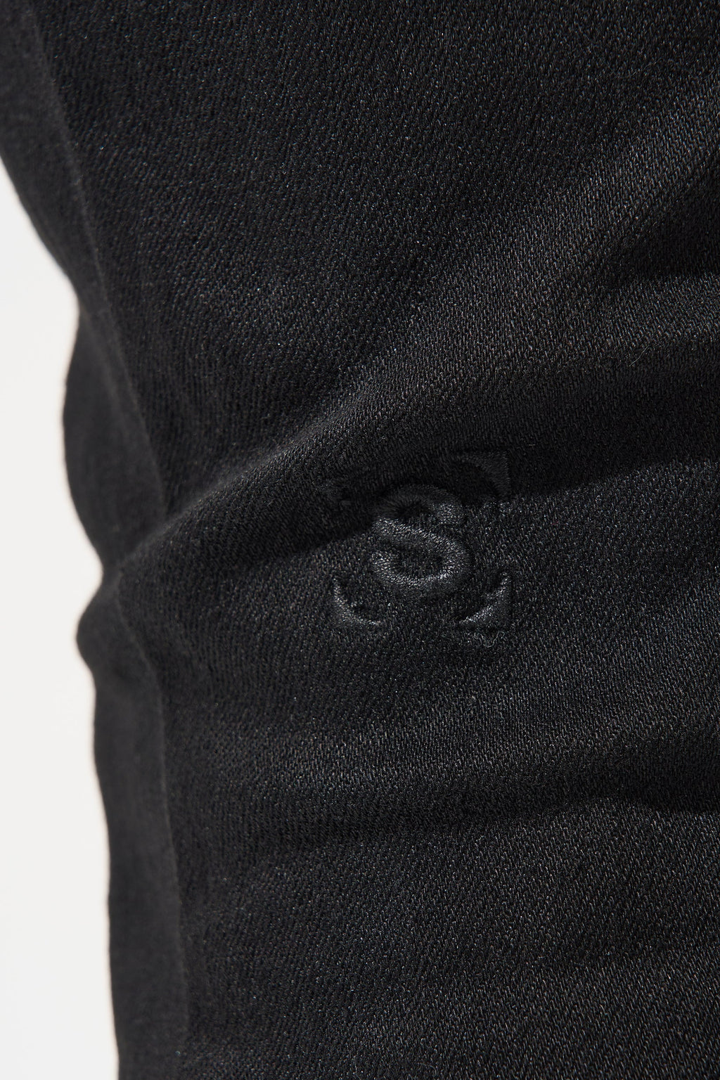 Black denim jeans close-up with embossed logo on the knee