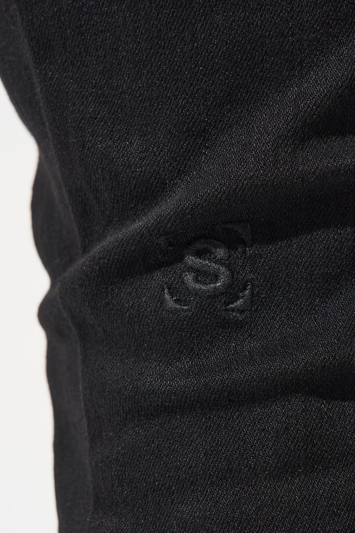 Black denim jeans close-up with embossed logo on the knee