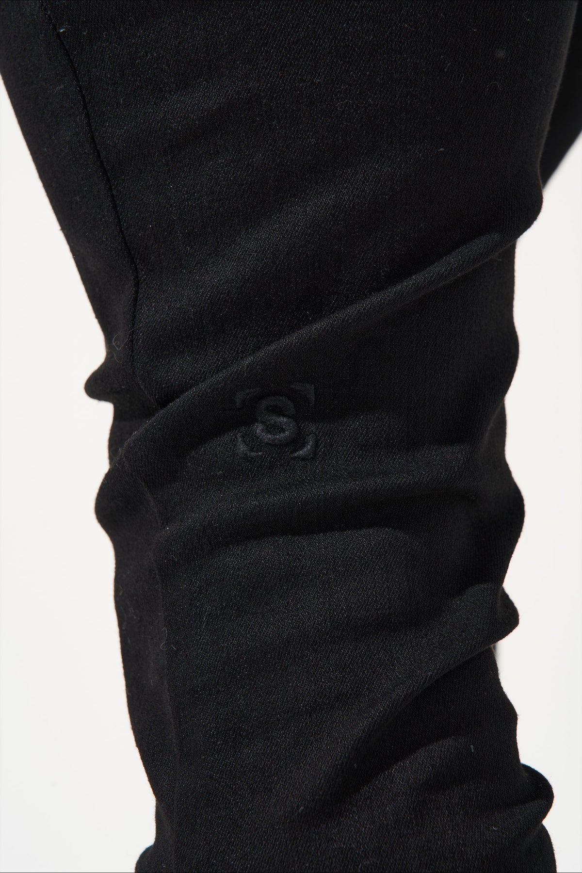 Men's dark jeans close-up of knee cuff with embossed S logo on wrinkled fabric