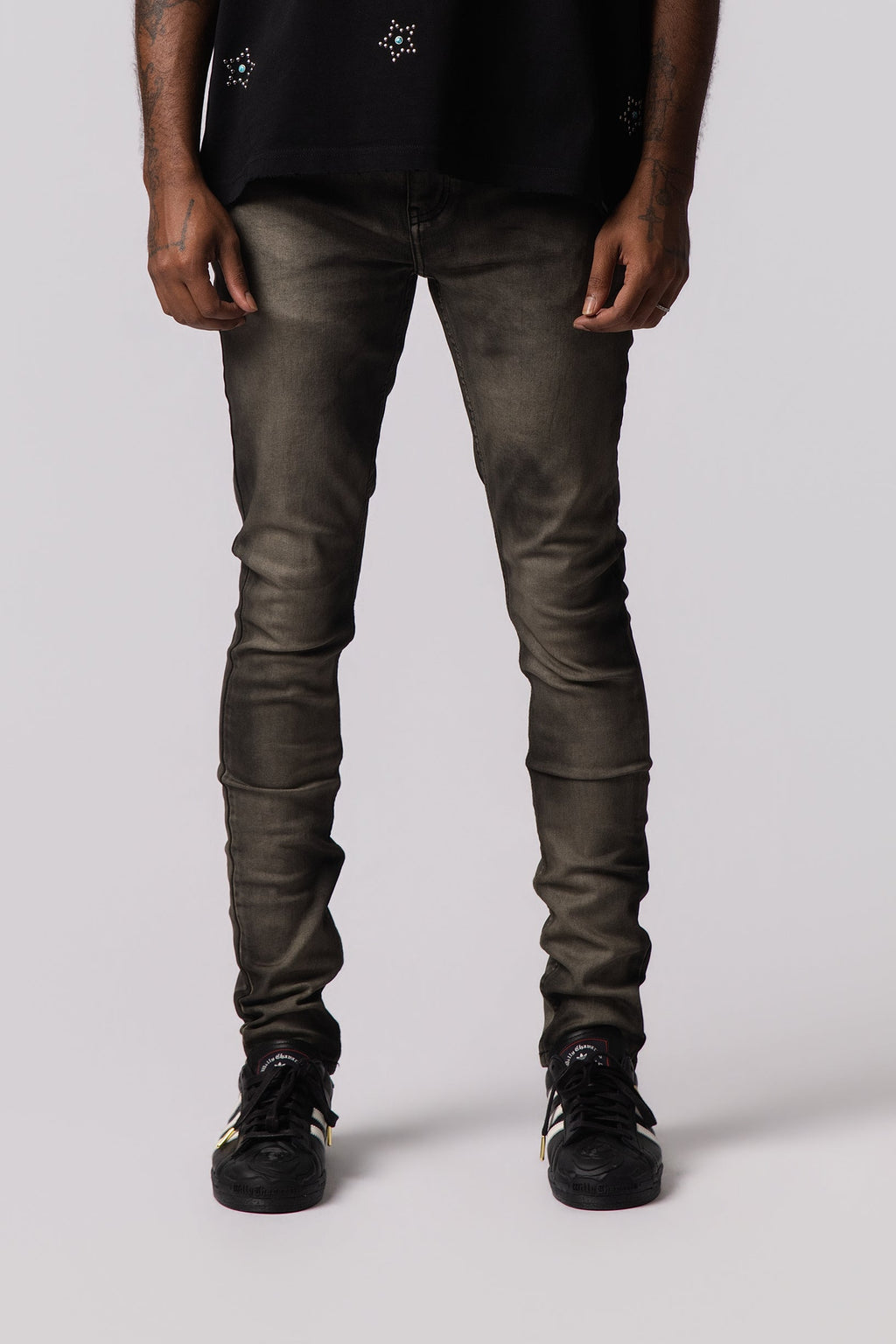 Men's olive-wash jeans, slim fit with tapered legs and dark sneakers.
