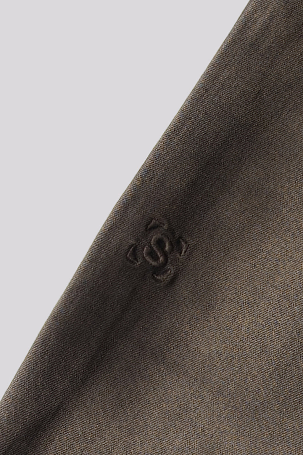 Olive denim fabric close-up with small embossed logo on the seam.