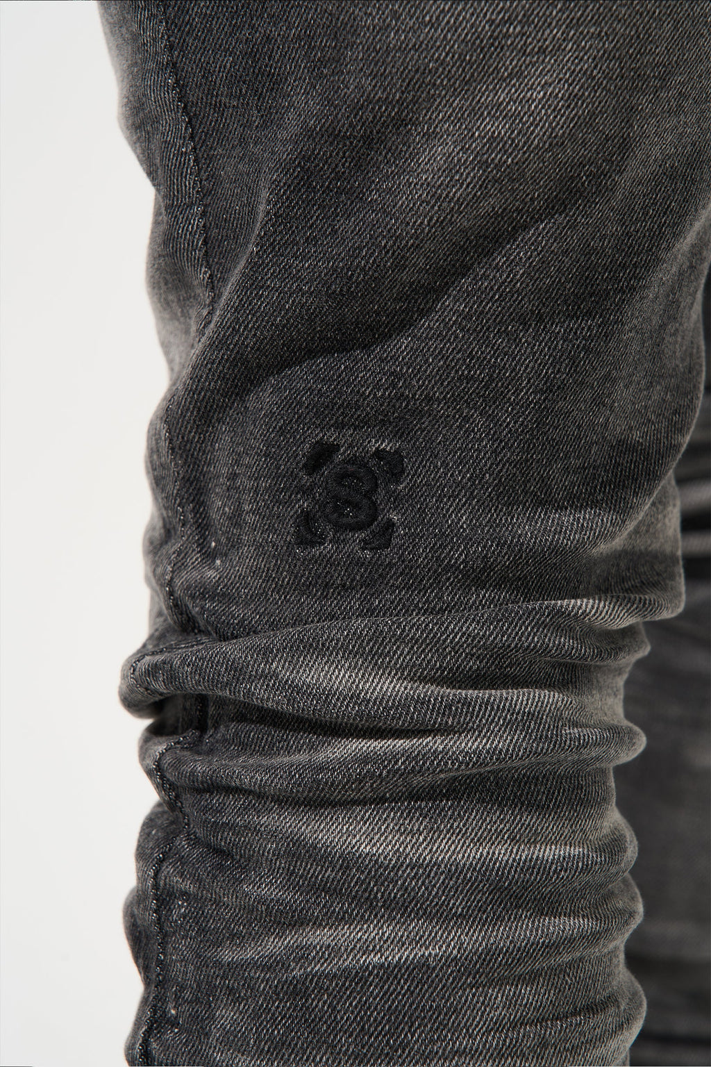 Men's dark gray jeans close-up with small stitched logo on leg