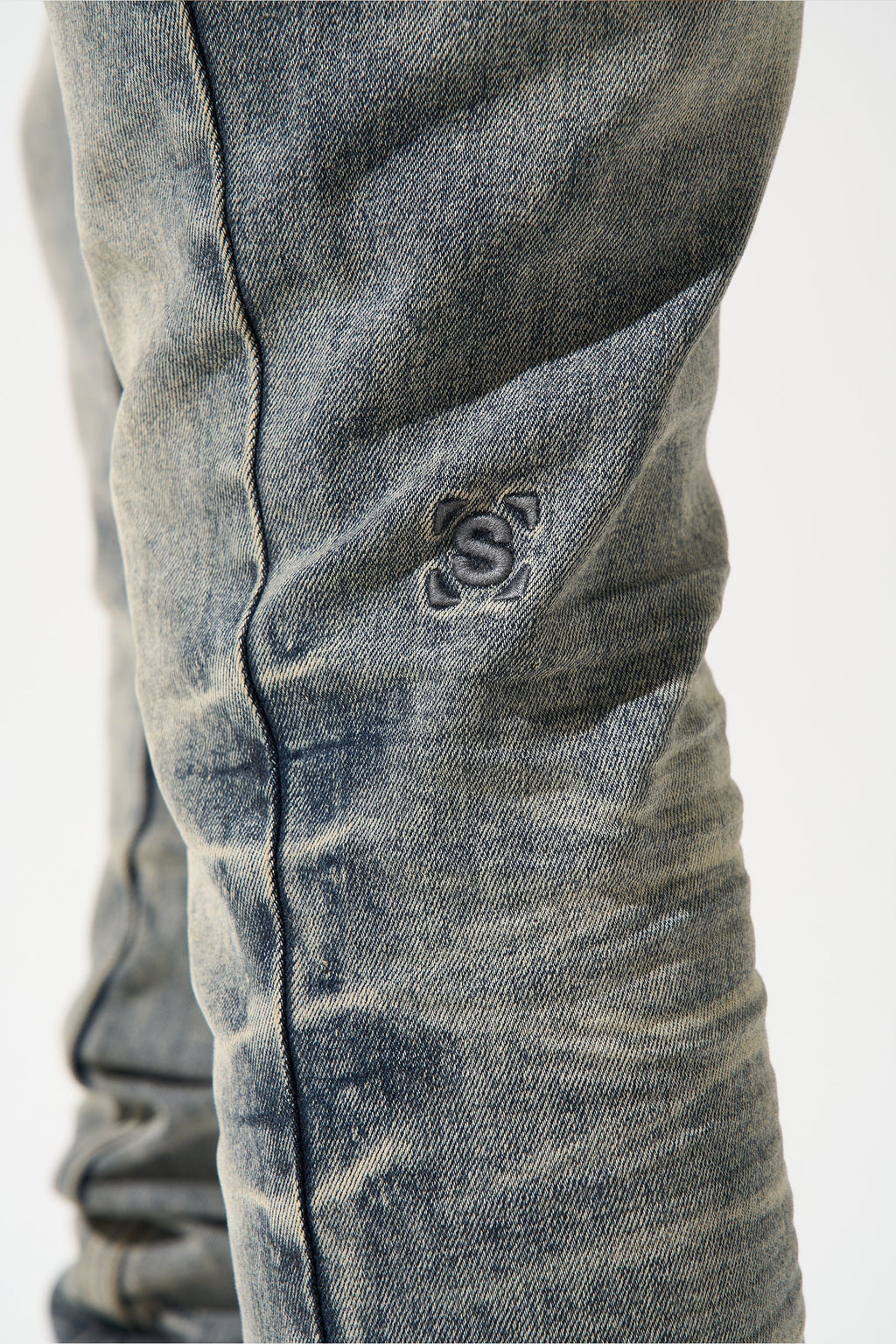 Men's gunmetal jeans leg with contrast logo patch and vertical seam stitching
