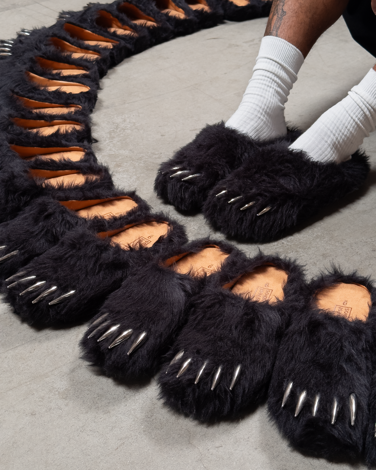 Black faux-fur bear claw mules close-up, spike claws and tan footbeds visible