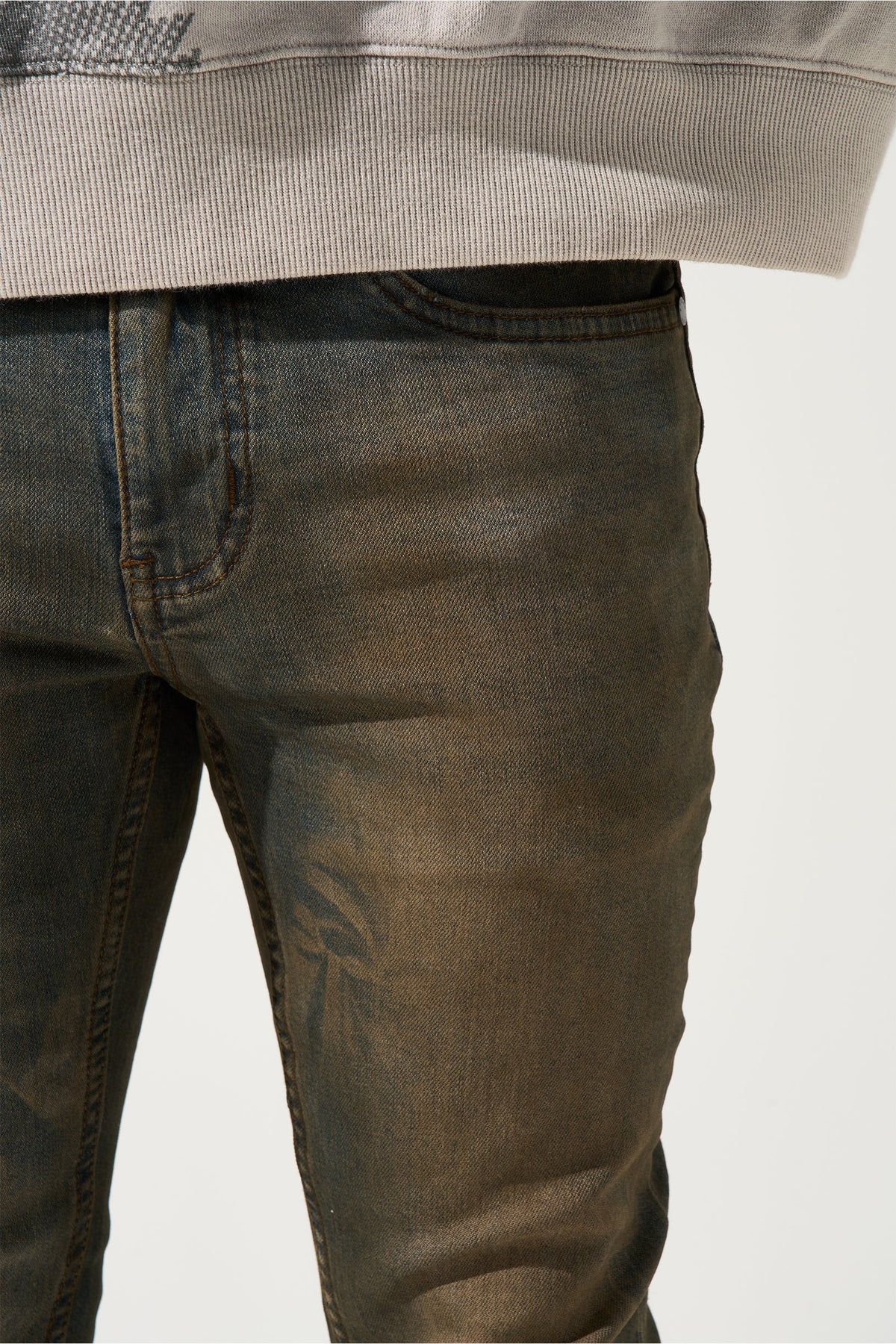 Earth-brown denim jeans close-up of waistband and topstitching.