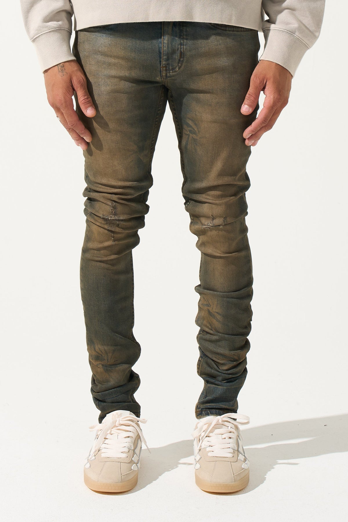 Earth-brown men's slim jeans with five-pocket front and ruched knee detail.