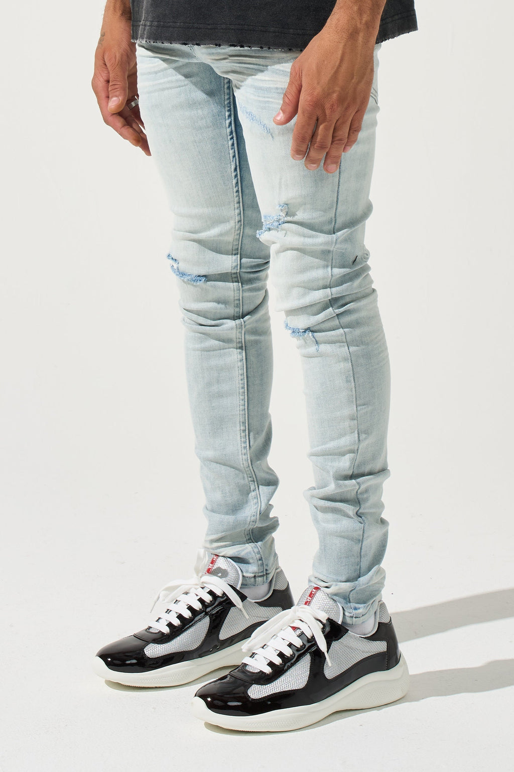Light blue distressed men’s jeans with whiskering, seam creases, and knee patches