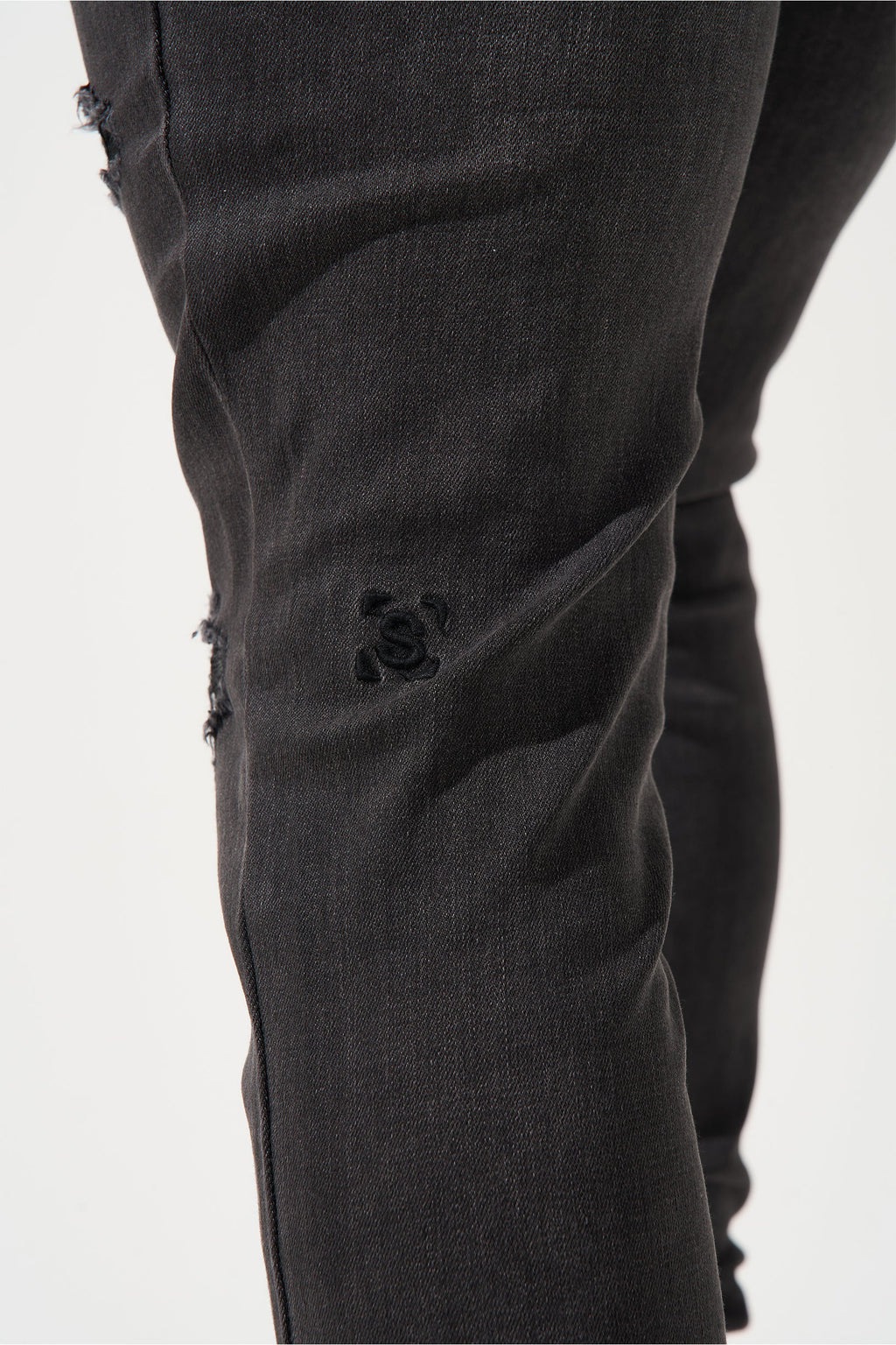 Men's charcoal jeans close-up of logo on thigh with dark wash wrinkles