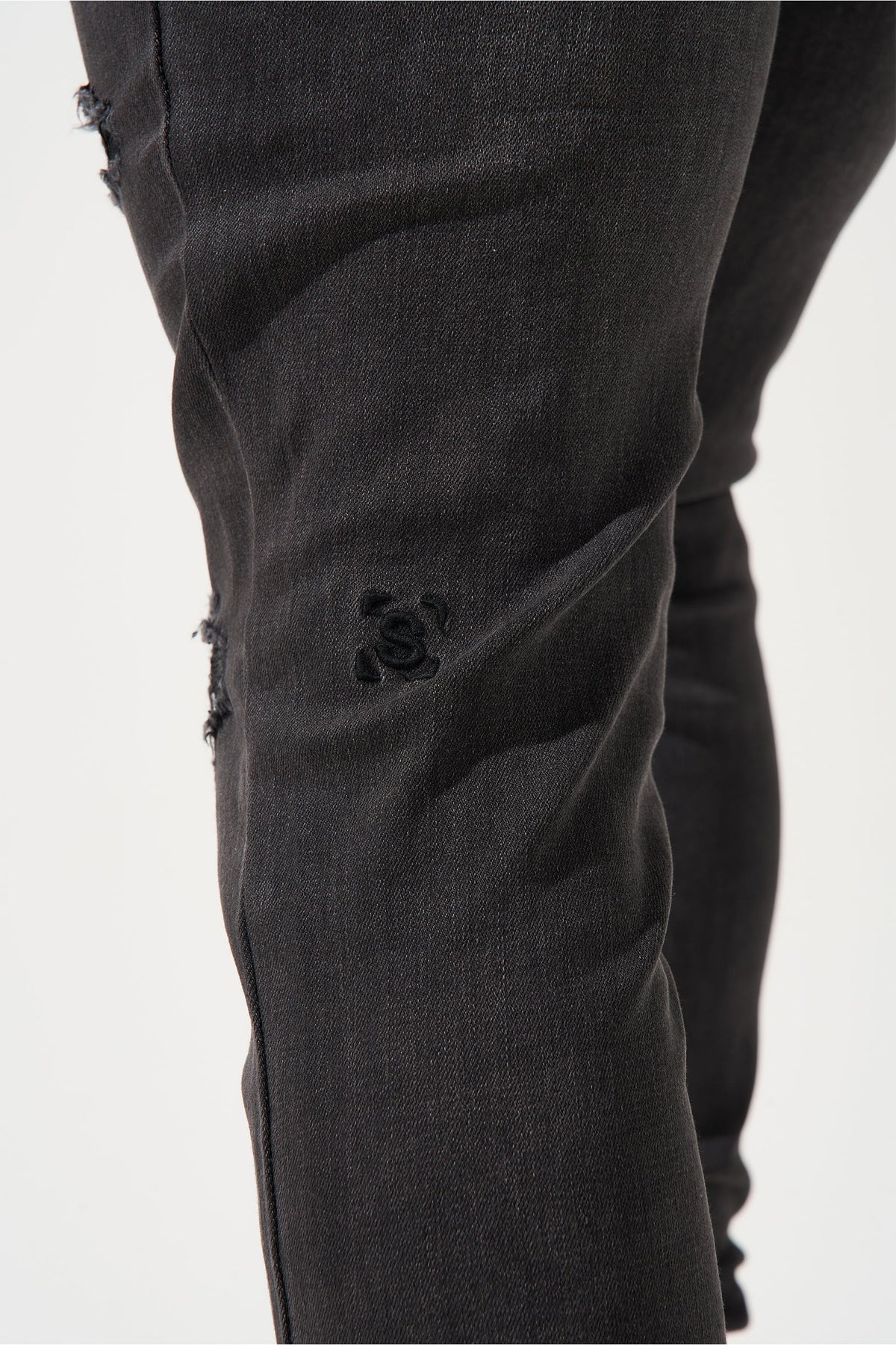 Men's charcoal jeans close-up of logo on thigh with dark wash wrinkles