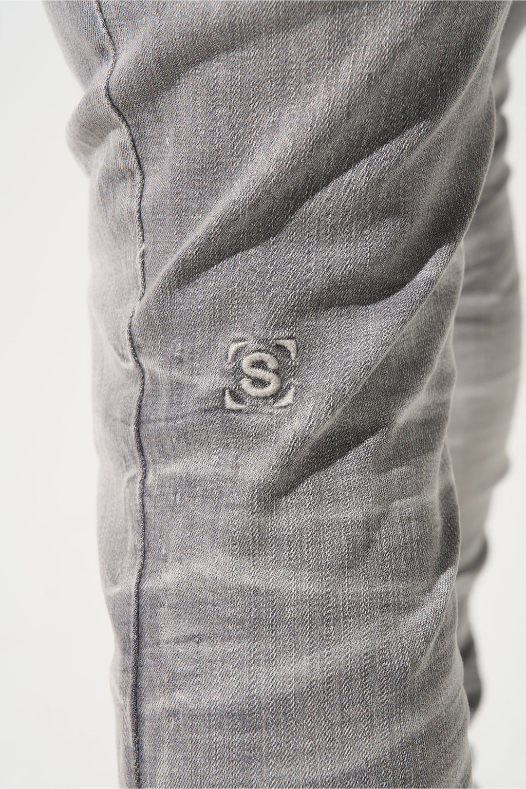 Grey men’s jeans close-up: embroidered S logo on the leg
