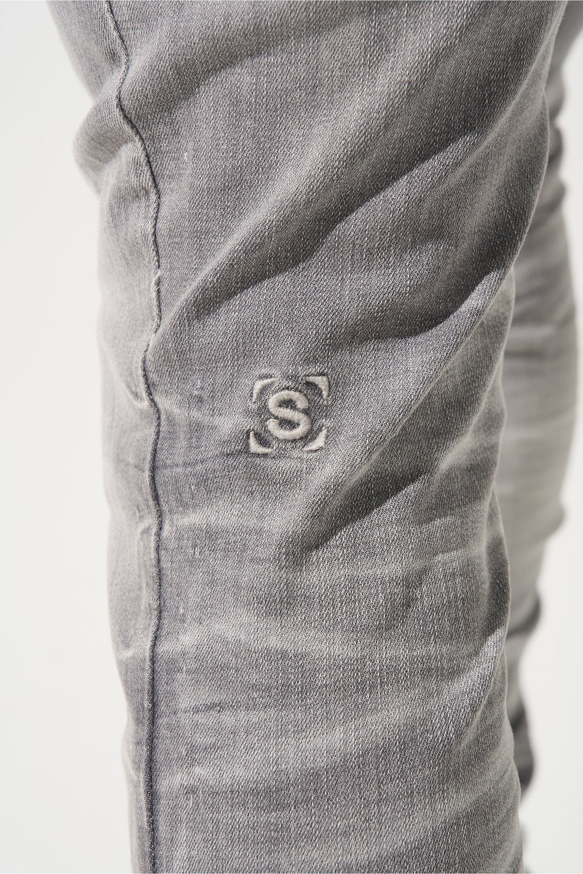 Grey men’s jeans close-up: embroidered S logo on the leg