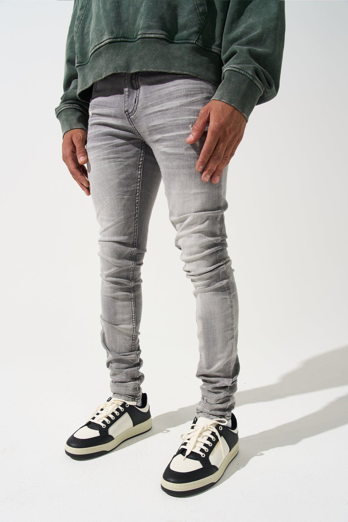Grey men’s jeans with ruched knees and black-and-cream lace-up sneakers