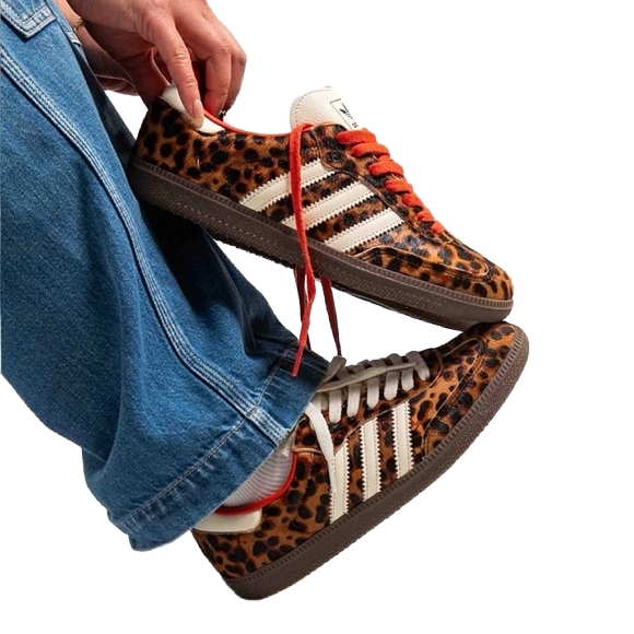 Leopard-print Adidas Samba OG sneakers with red lace-up, held near blue jeans