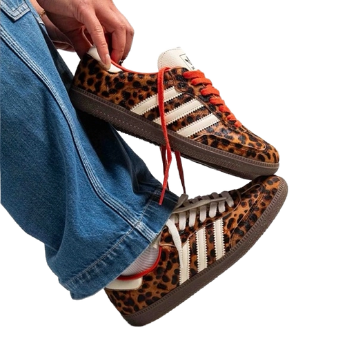 Leopard-print Adidas Samba OG sneakers with red lace-up, held near blue jeans